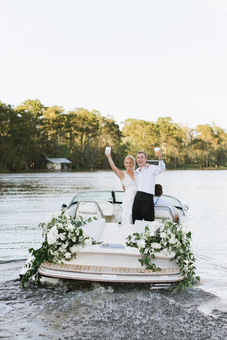 a bride and groom are on a boat in the water with greenery around them