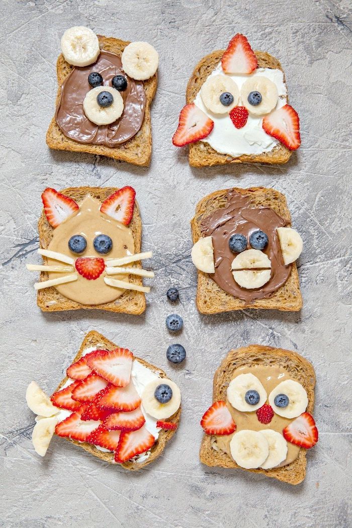 four slices of toast with fruit and chocolate on them, each decorated like a cat