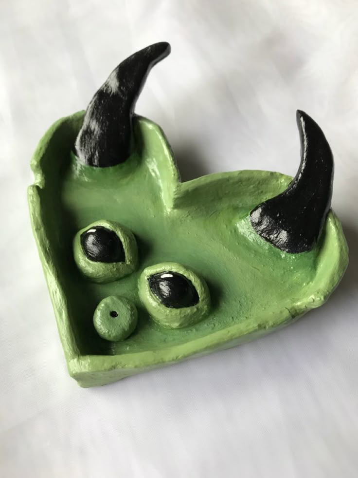 a green ceramic object with black horns and eyes