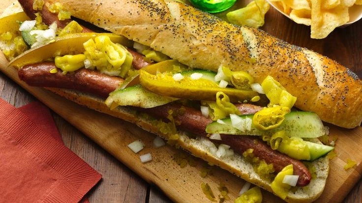 a hot dog with toppings on a cutting board next to chips and a bottle