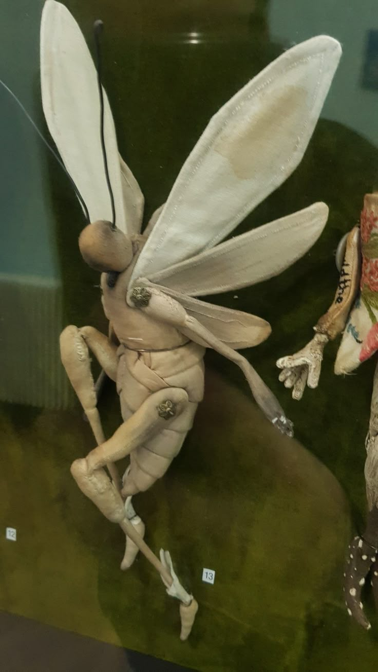 two figurines are on display in a glass case, one is dressed as a fairy