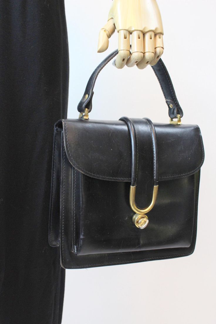 Gorgeous 1950's Ronora handbag! Done in a glossy black leather with gold hardware. The flap bag has a strap that fits into the twist lock. Two inner sections, one inner zipper pouch and one outer pouch. Brand: Ronora Color: black Material:  leather Condition: Very Good Vintage: Some light scuffs on the glossy leather. ✂-----Measurements  Length: 9" Width: 3" Height: 8" Total height w/ strap : 12" Top Handle Bags, Handbag Purse, Flap Bag, Leather Handbag, Zipper Pouch, Gold Hardware, Purses And Handbags, Top Handle, Leather Handbags