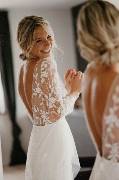 a woman standing in front of a mirror wearing a white dress and holding her hands together