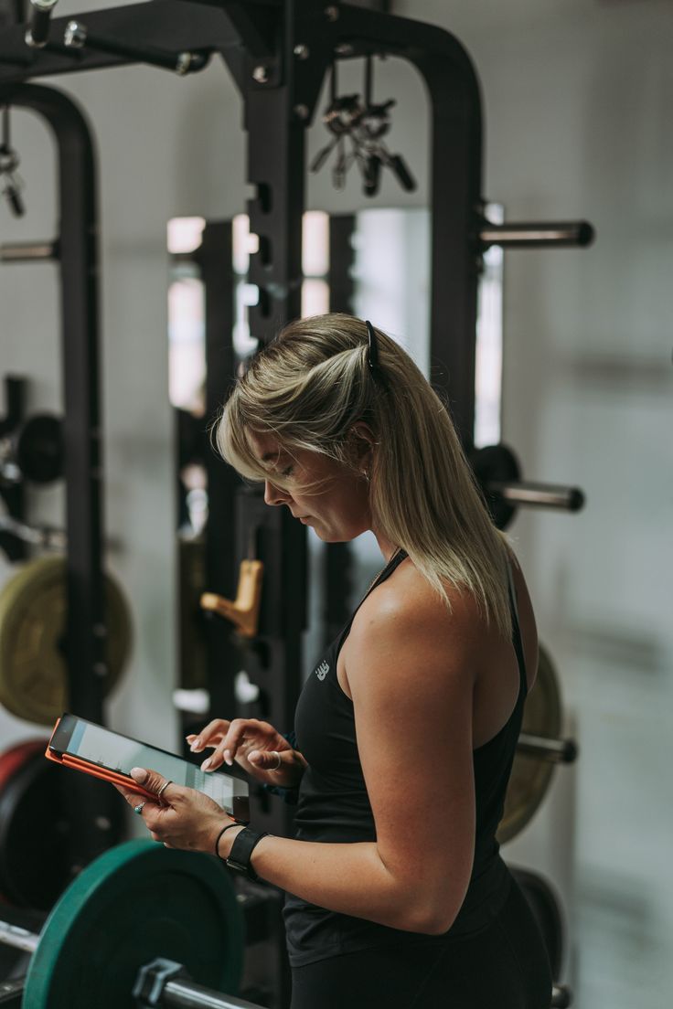 a woman standing in front of a gym machine looking at her digital tablet computer screen