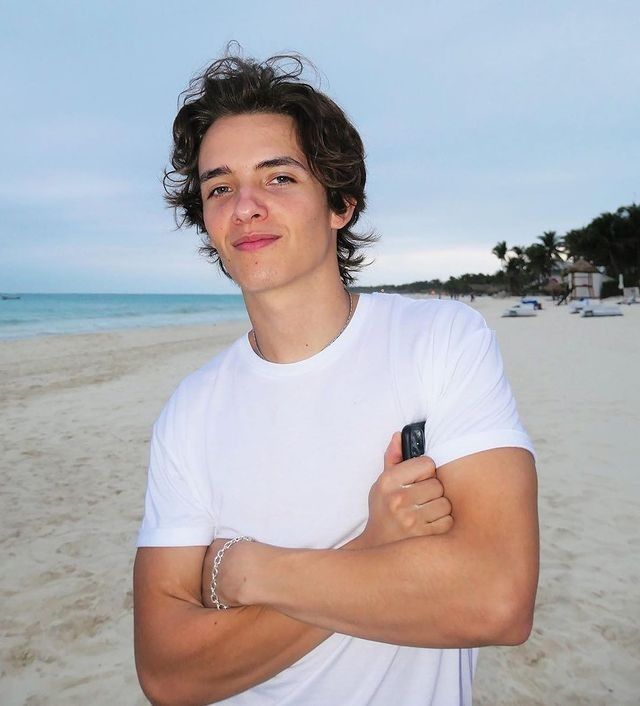 a young man is standing on the beach with his arms crossed and looking at the camera