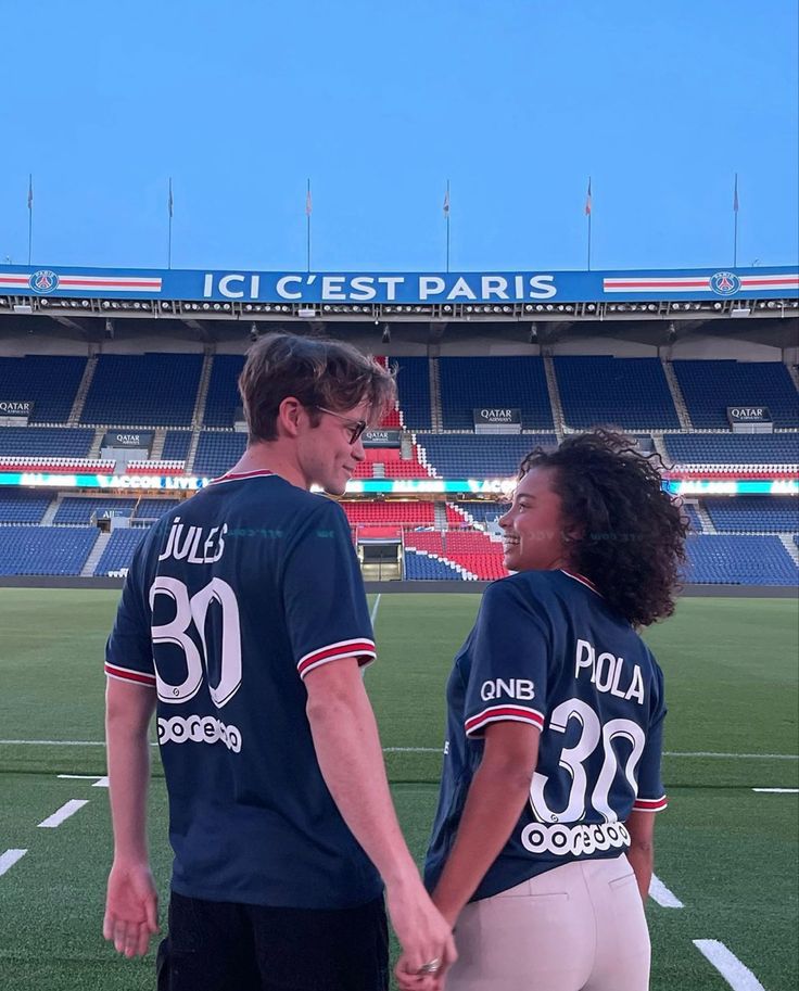 two people standing in front of a soccer field holding hands and smiling at each other