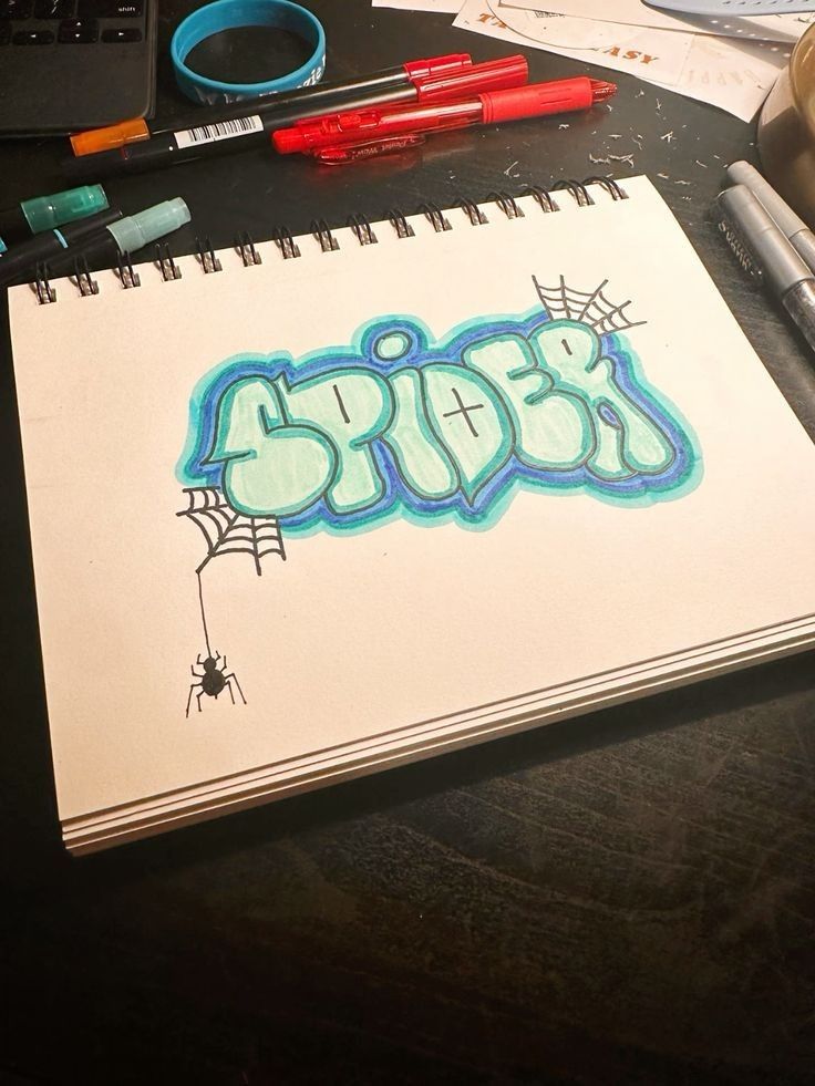 a notebook with the word spider written in blue ink on it next to markers and pens