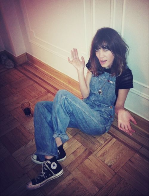 a woman sitting on the floor with her hands up in front of her face and wearing overalls