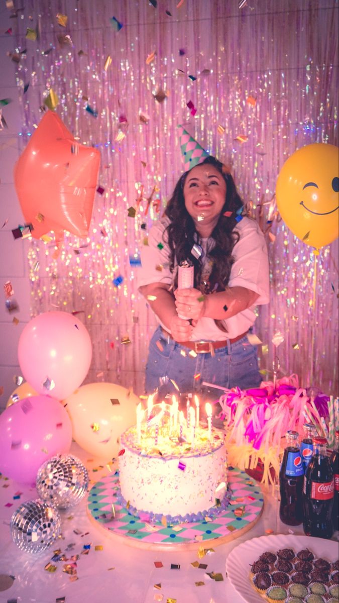 a woman standing in front of a cake surrounded by balloons and confetti on the table