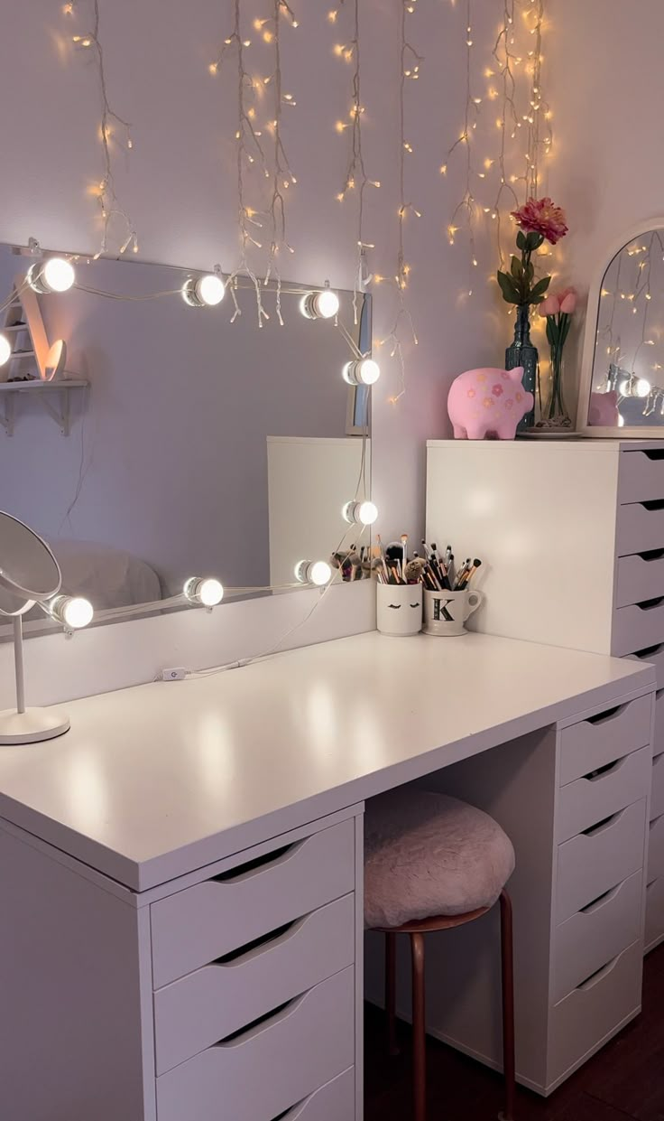 a white vanity with lights hanging from it's ceiling and a stool in front of it