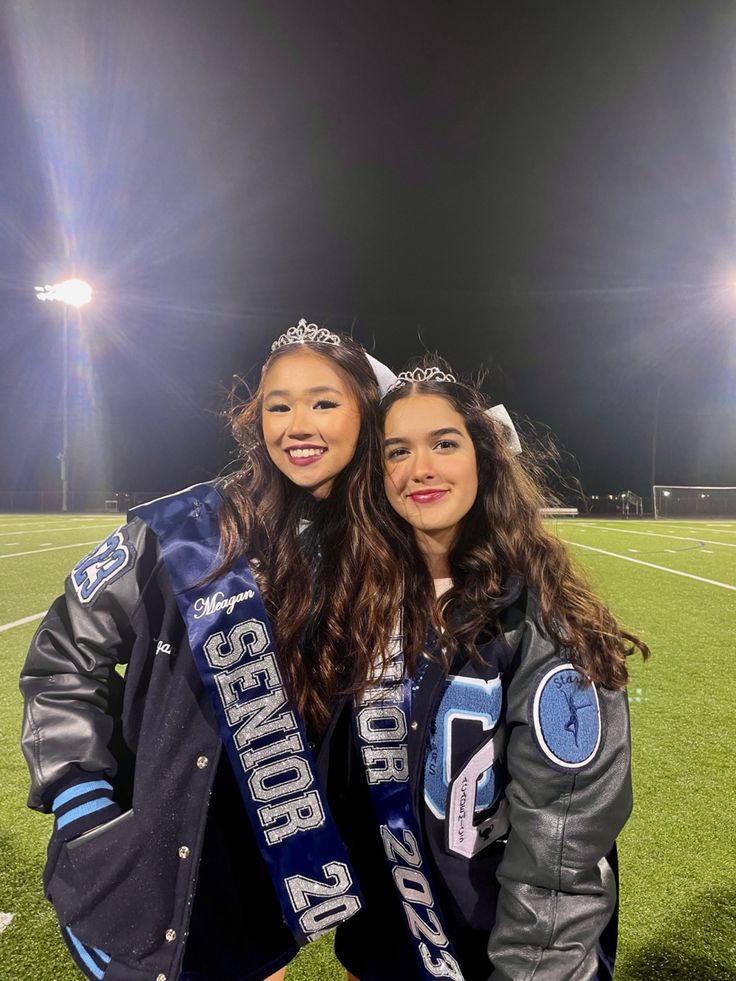 two young women standing next to each other on top of a soccer field at night