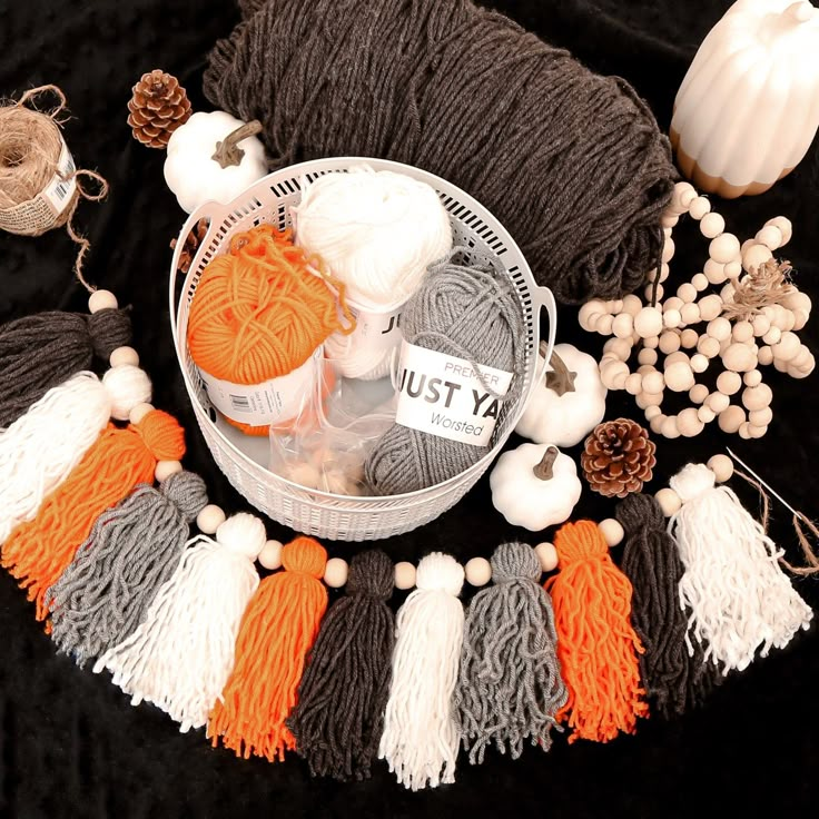 yarn, needles and balls of yarn are arranged on a black tablecloth with white pumpkins