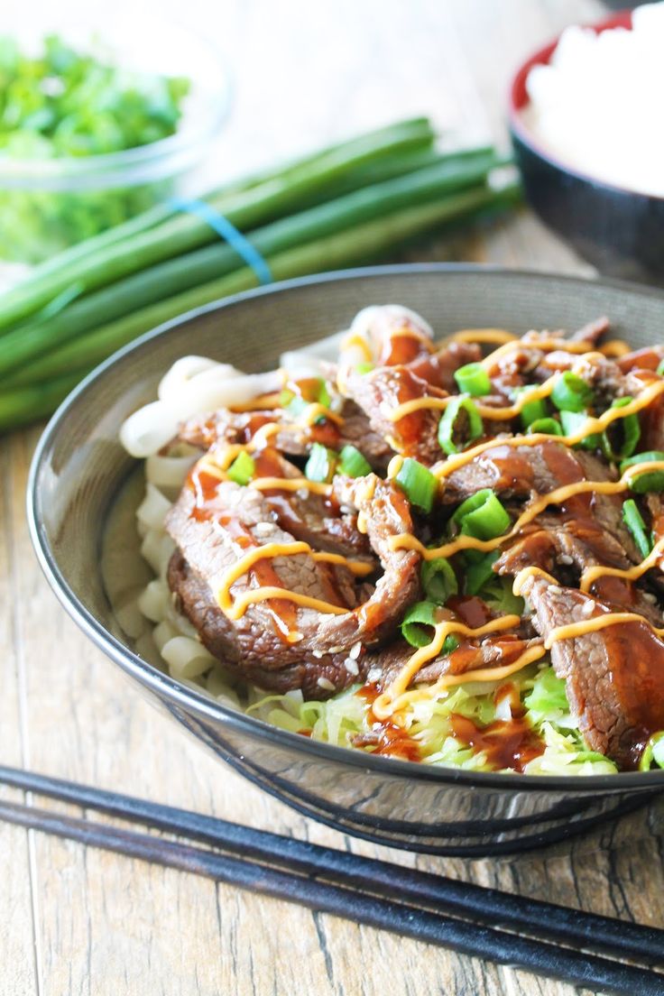 a bowl filled with meat and vegetables on top of rice next to chopsticks