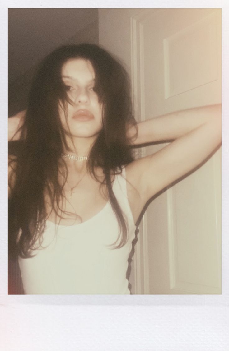 a woman with long hair standing in front of a door wearing a white tank top