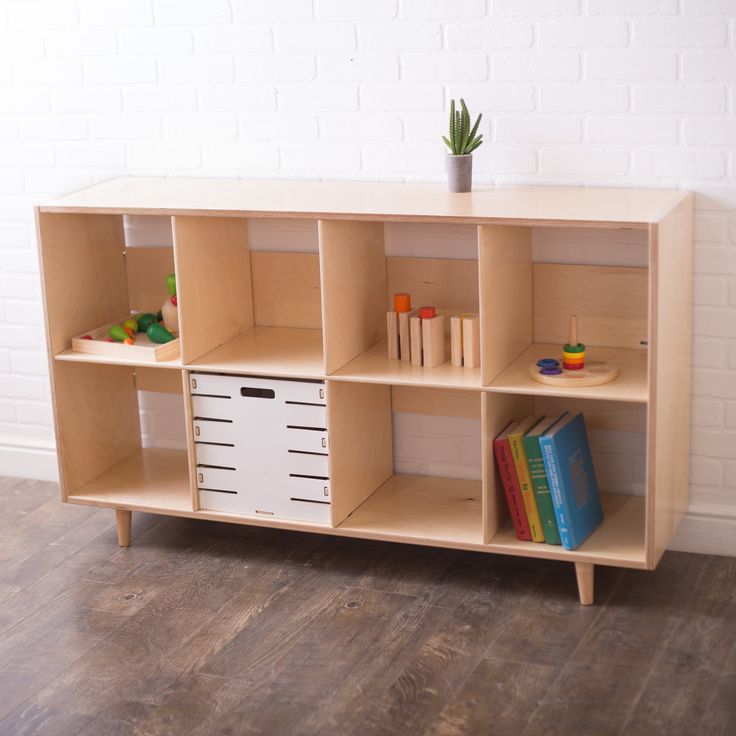 a wooden shelf with books and toys on it in front of a white brick wall