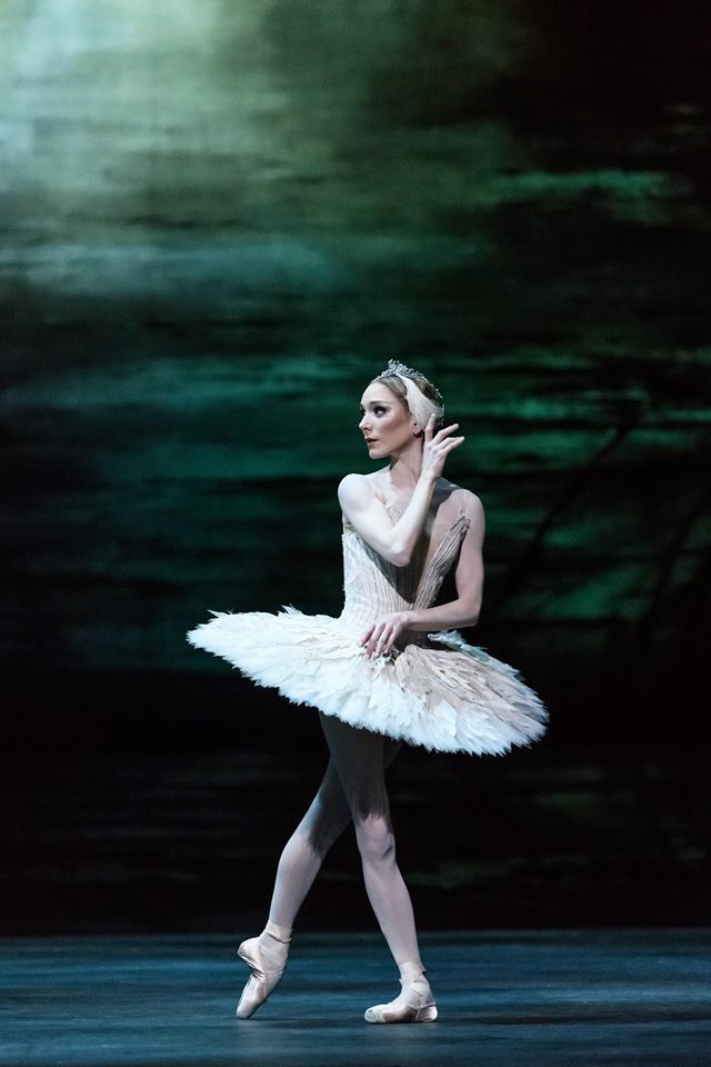 a ballerina in white tutu with her arms behind her head and one leg bent forward