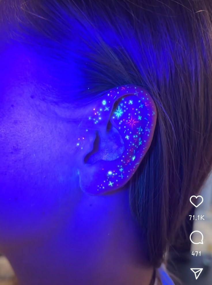 a girl with blue and purple glow in her ears, looking at the stars on her ear