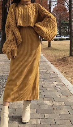 a woman is standing on the sidewalk wearing a brown sweater and skirt with white boots