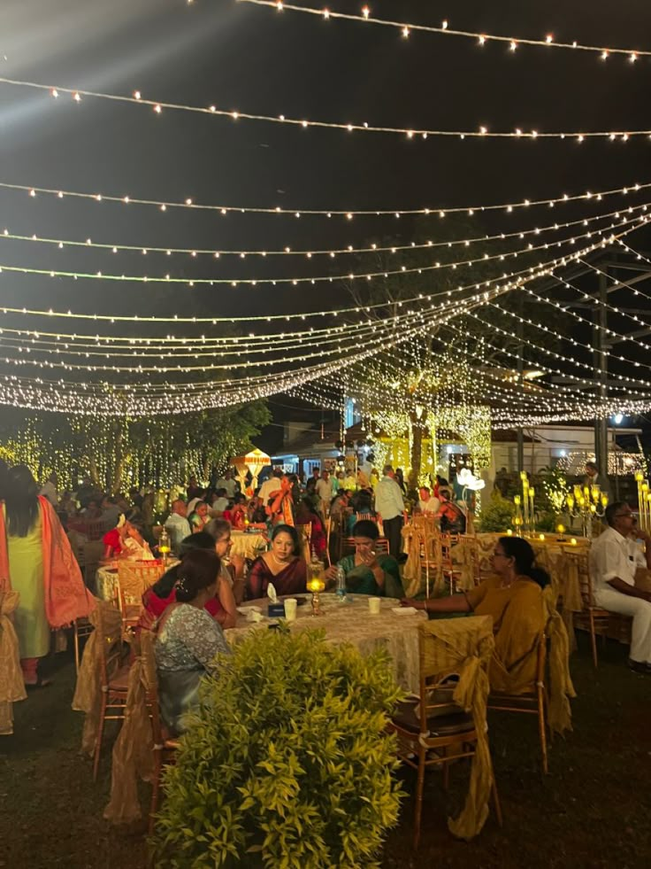 people sitting at tables under string lights in an outdoor area with white linens strung across the ceiling