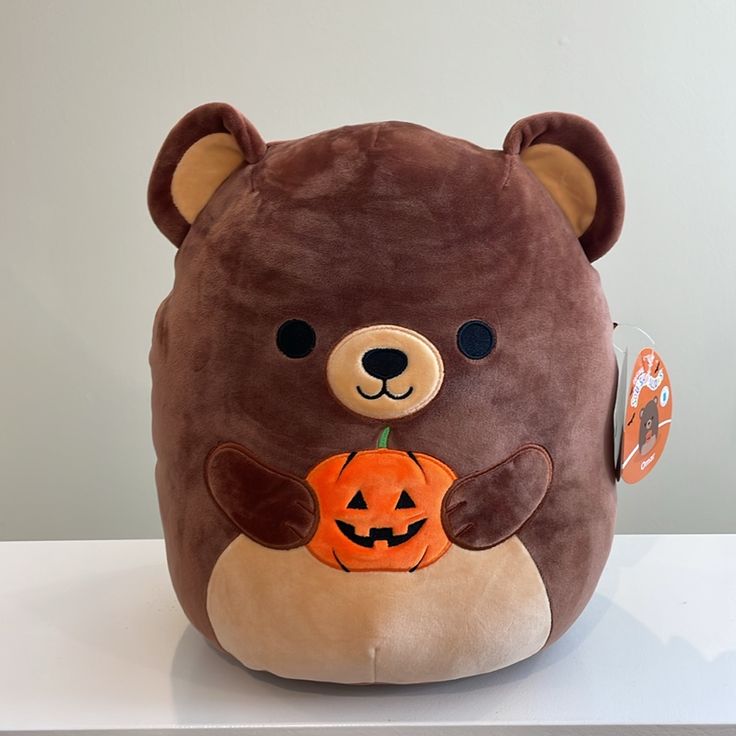 a brown teddy bear with a pumpkin in its mouth sitting on top of a table