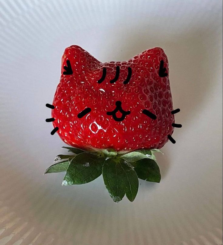 a strawberry shaped like a cat sitting on top of a green plant