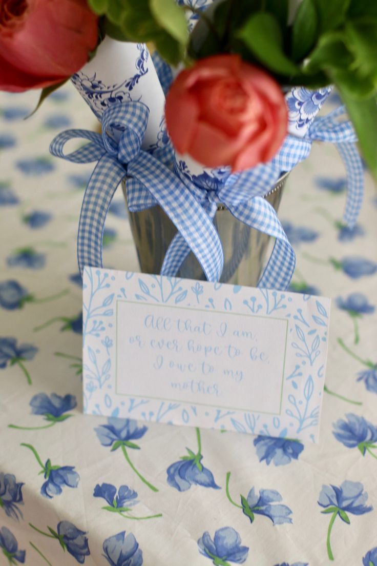 a vase filled with red and pink flowers on top of a blue table cloth covered table