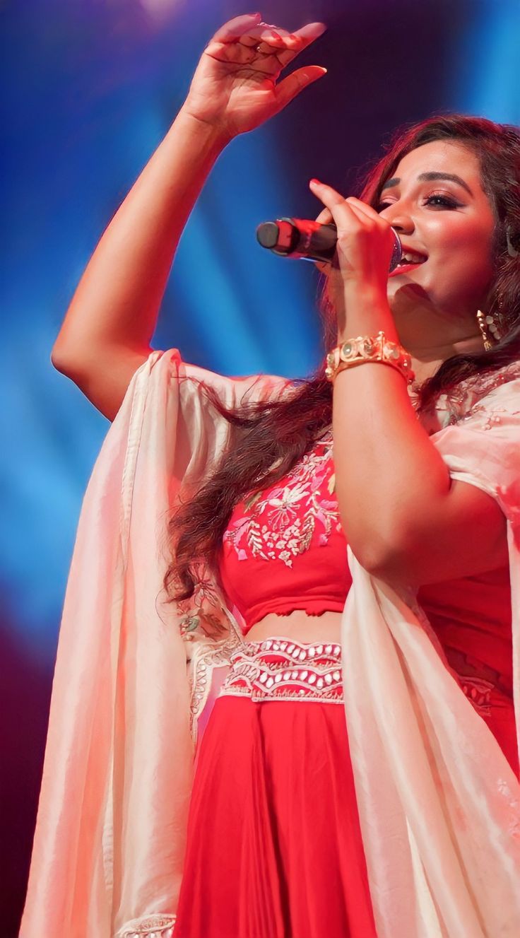 a woman in a red and white outfit singing into a microphone with her hands up