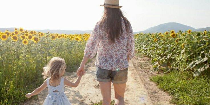 a mother and daughter walking down a dirt road in a field with sunflowers