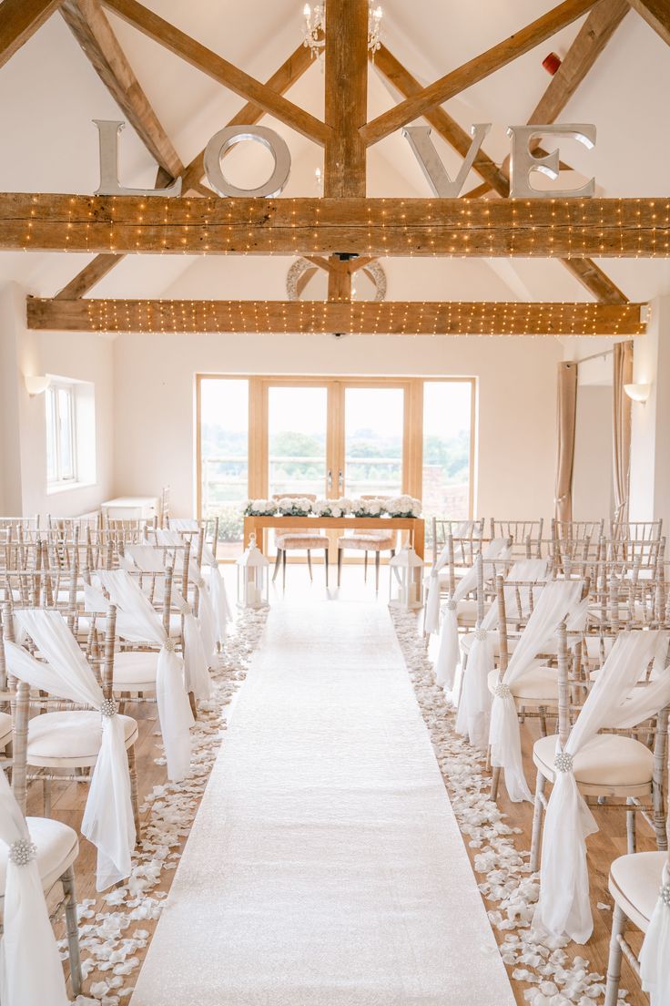 an indoor wedding venue with white chairs and aisle leading to the ceremony room, decorated with lights