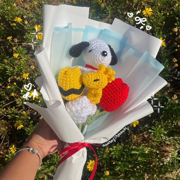 a person holding a bunch of crocheted stuffed animals in their hands with flowers behind them