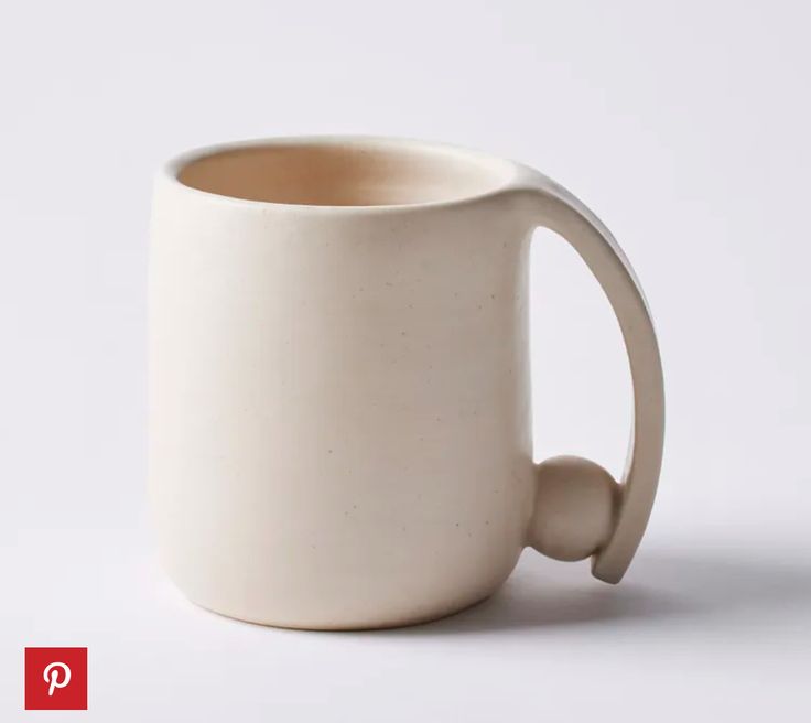 a white coffee mug with a handle is shown on a plain surface, and has a red q in the middle