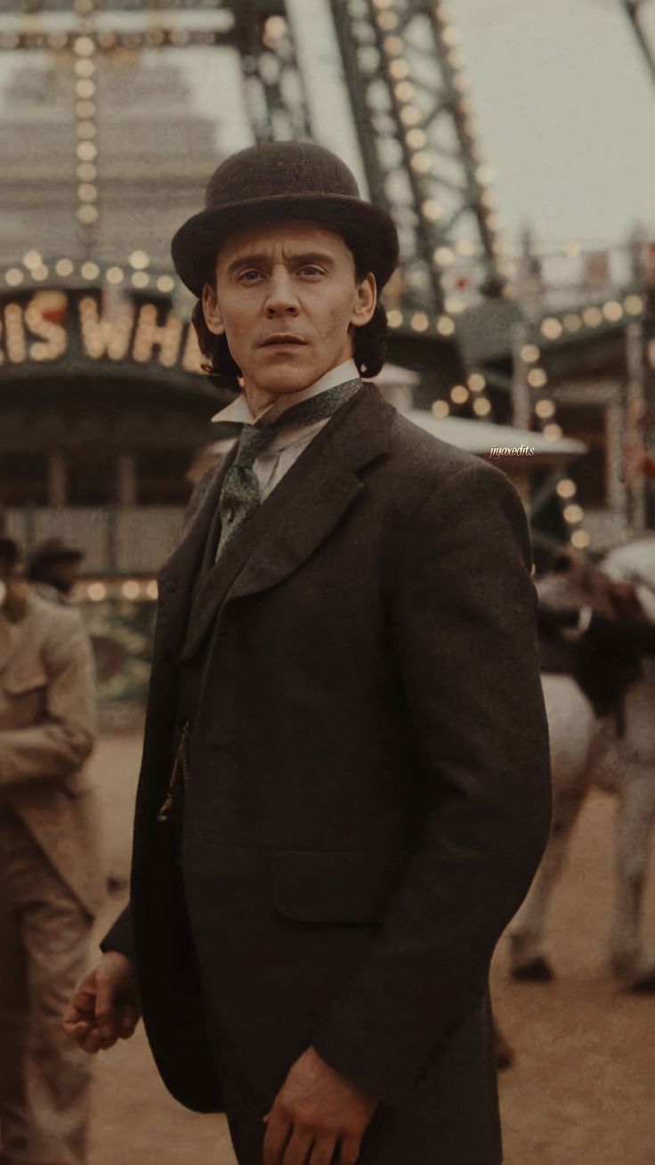 a man in a suit and hat standing next to a carnival ride at an amusement park