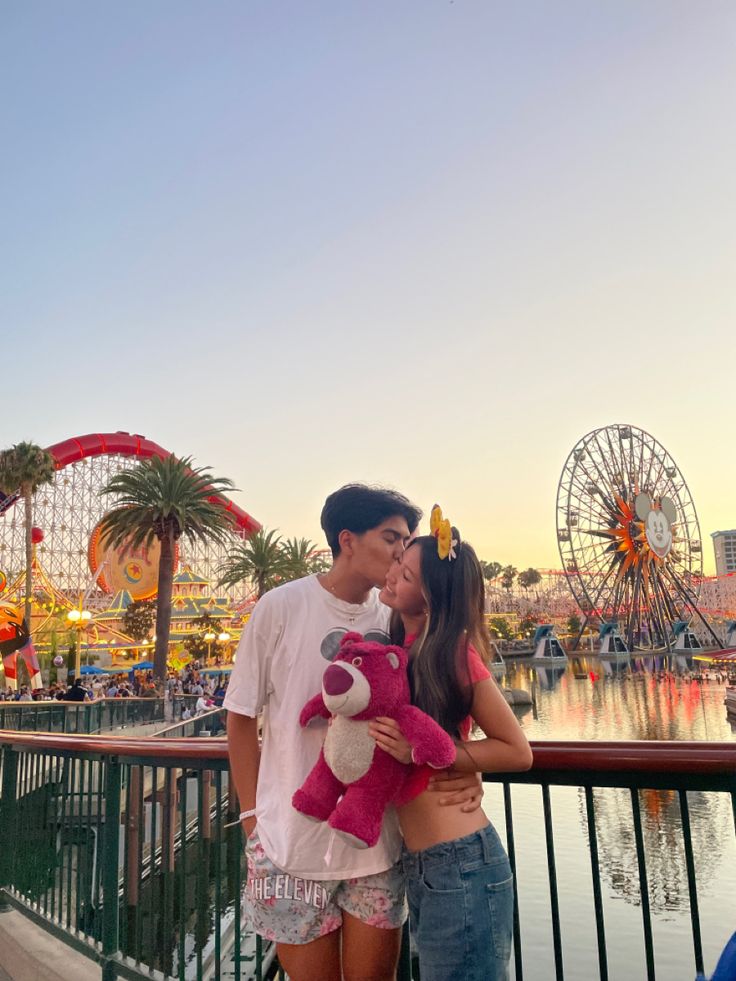 a man and woman standing next to each other in front of a ferris wheel at an amusement park