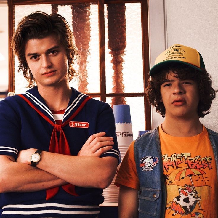 two young men standing next to each other in front of a window with their arms crossed