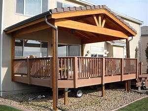 a covered patio with wooden railings next to a house