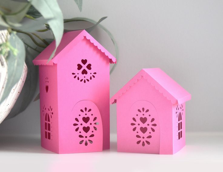 two pink paper houses sitting on top of a table next to a potted plant