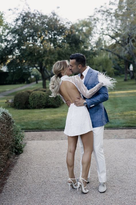 a man and woman are kissing in front of some trees on the sidewalk with their arms around each other