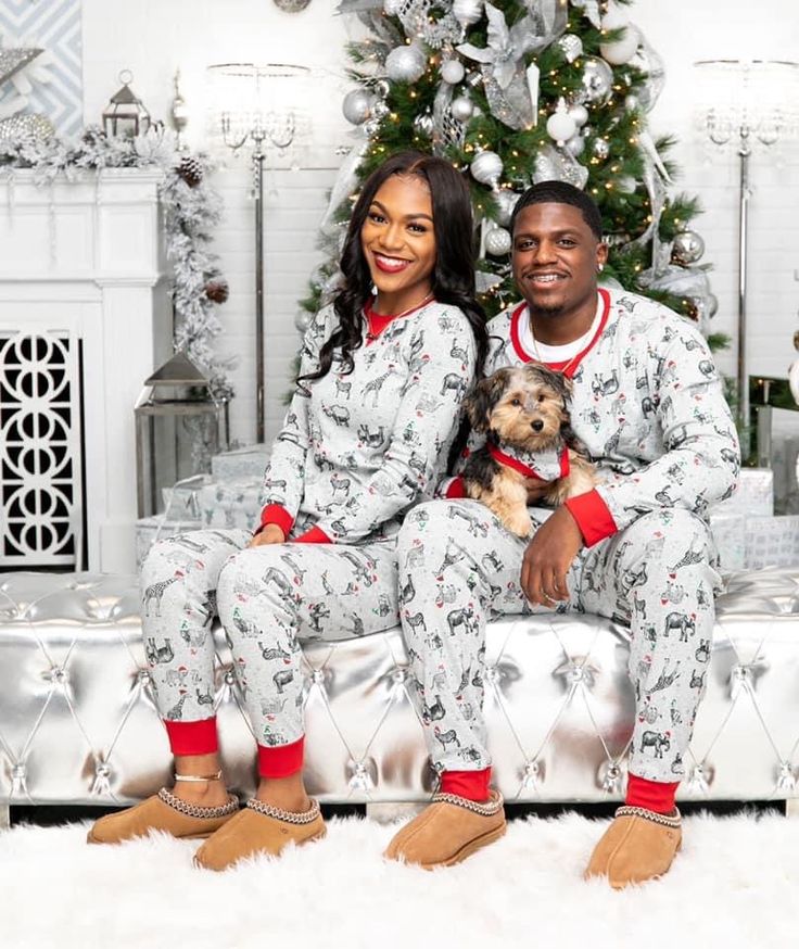 a man and woman in matching christmas pajamas sitting on a couch with a small dog