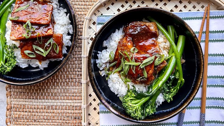 two plates filled with meat and rice on top of a table next to chopsticks