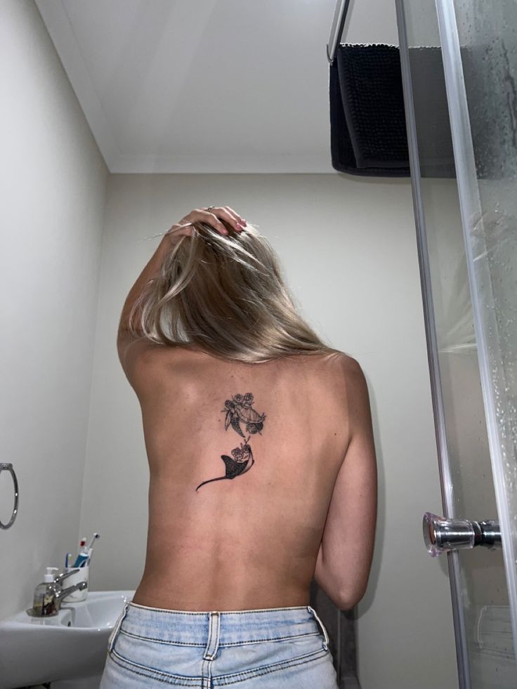 a woman with a flower tattoo on her back standing in front of a shower door