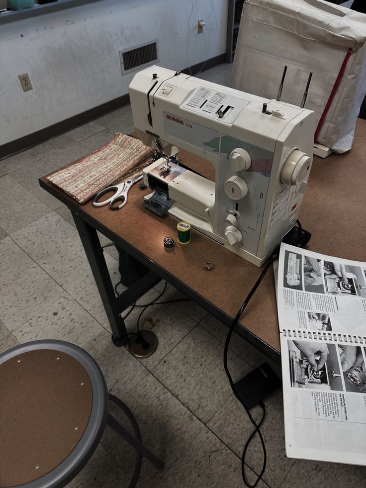 a sewing machine sitting on top of a wooden table next to a newspaper and chair