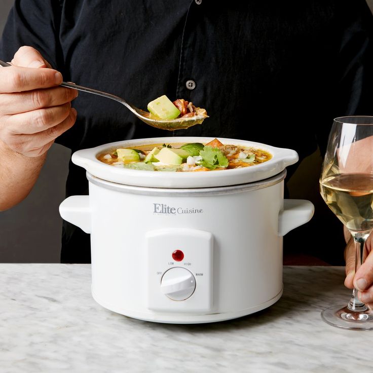 a man holding a spoon with food in it while eating from a slow cooker