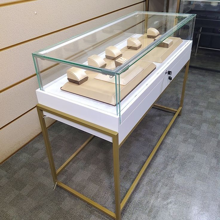 a glass display case with four pieces of jewelry on it in front of a wall