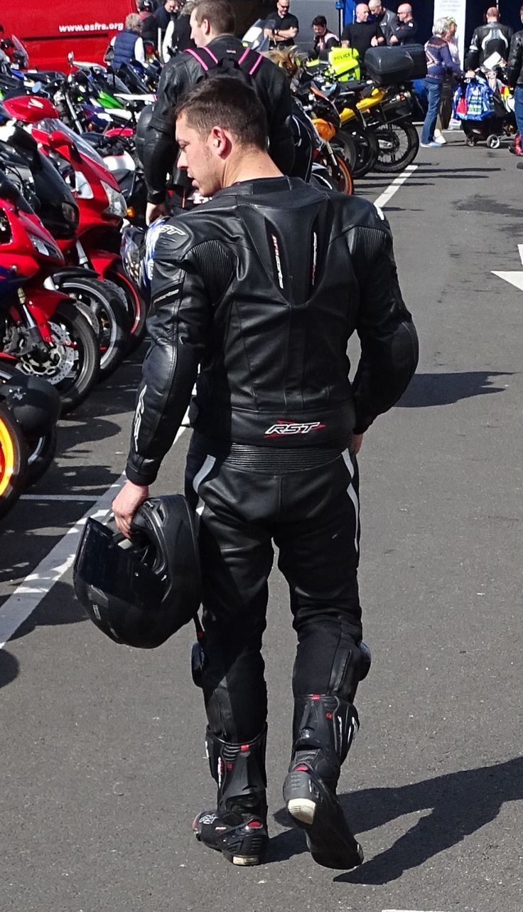 a man walking down the street with his motorcycle gear on and people in the background