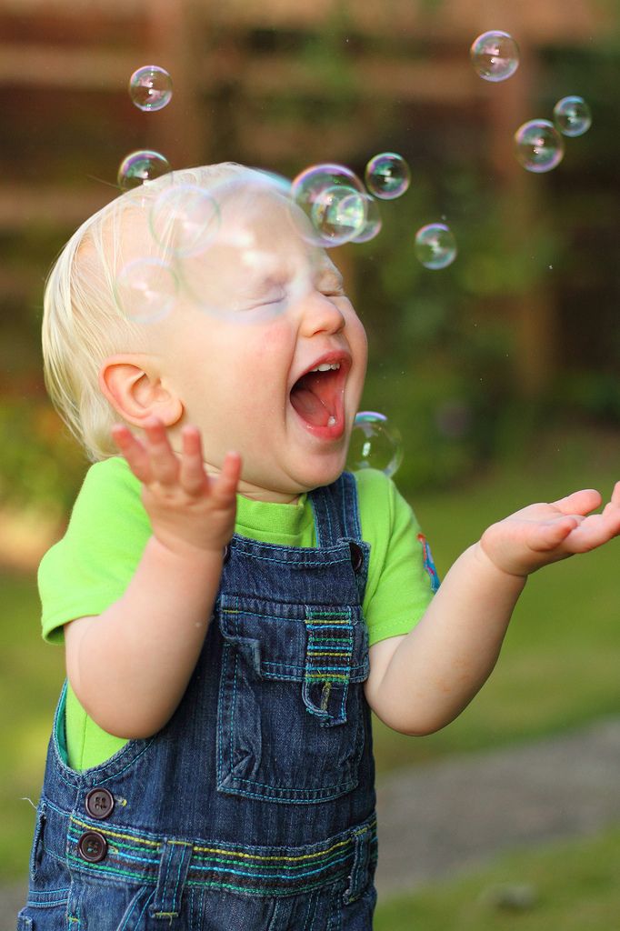 a little boy that is standing in the grass with soap bubbles flying around him and laughing