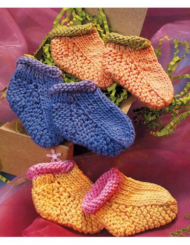 crocheted baby booties are displayed in front of a pink clothed background