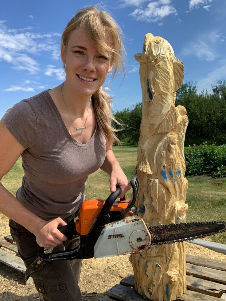 a woman holding a chainsaw next to a carved bear