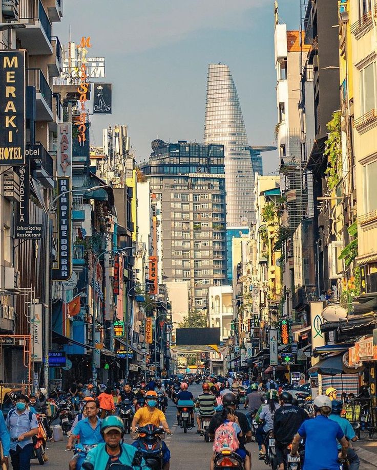 many people are riding motorcycles down the street with tall buildings in the backgrouds