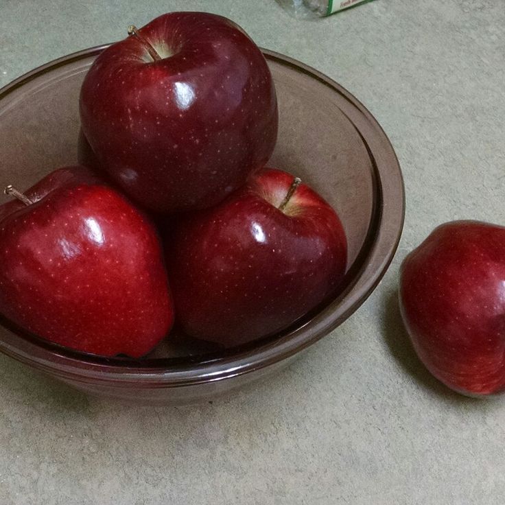 a bowl filled with red apples sitting on top of a counter