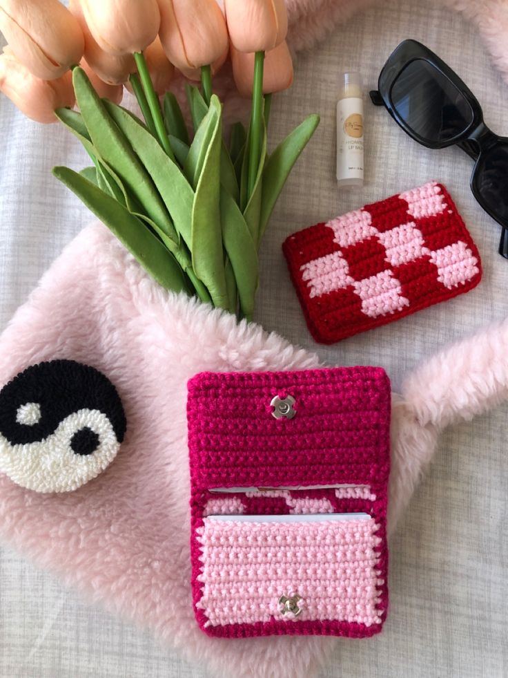 there are some crocheted items on top of a blanket next to flowers and sunglasses